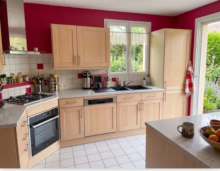 Photo prise pendant la visite : cuisine à rénover, meubles en bois clair et murs framboise
